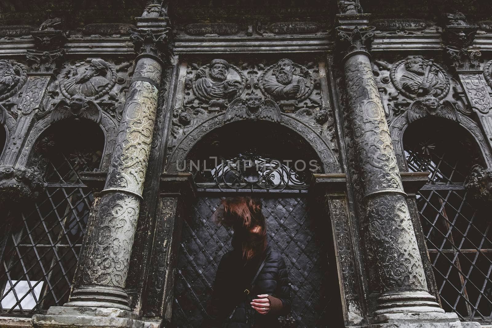 The young girl stands on the background of the old gothic wall.