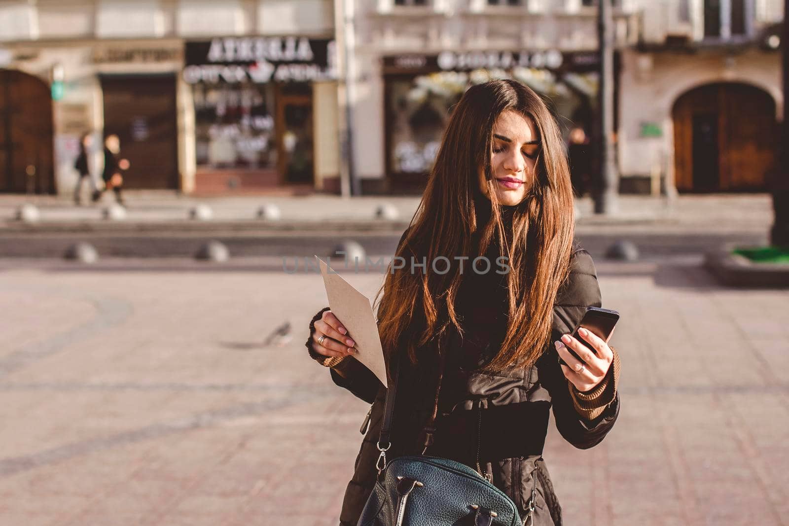 Young nice girl looks at the phone in the middle of a big city.