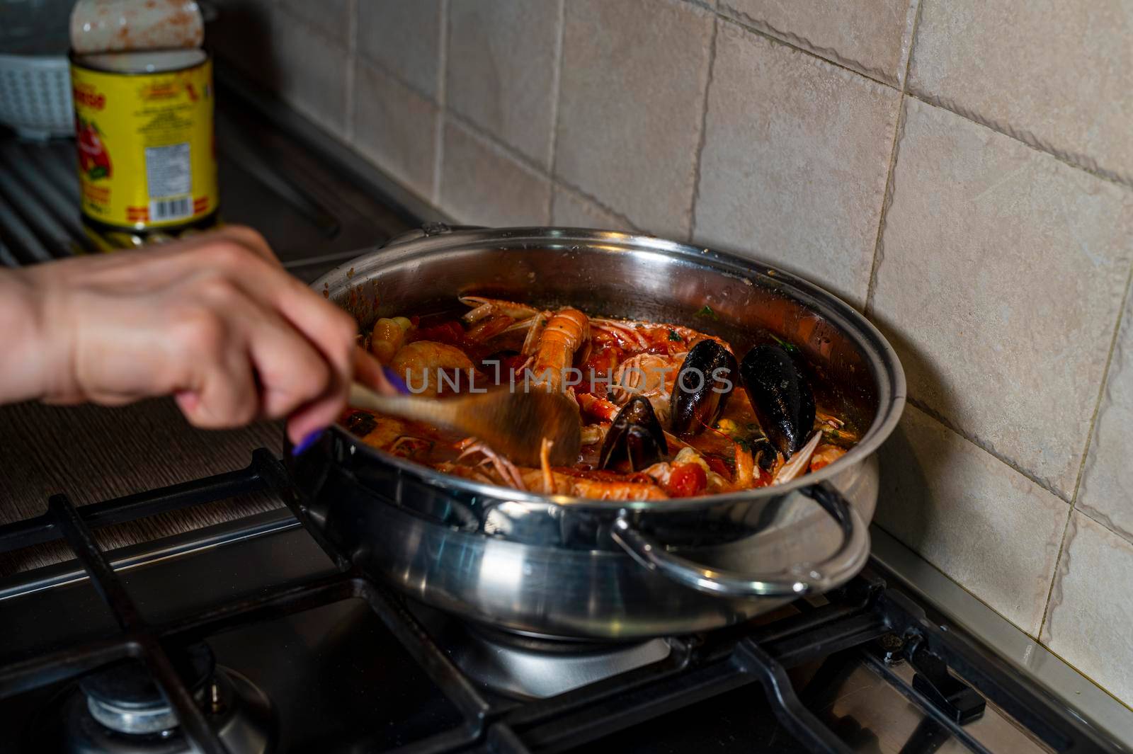 Man handling fish soup with wooden ladle while cooking