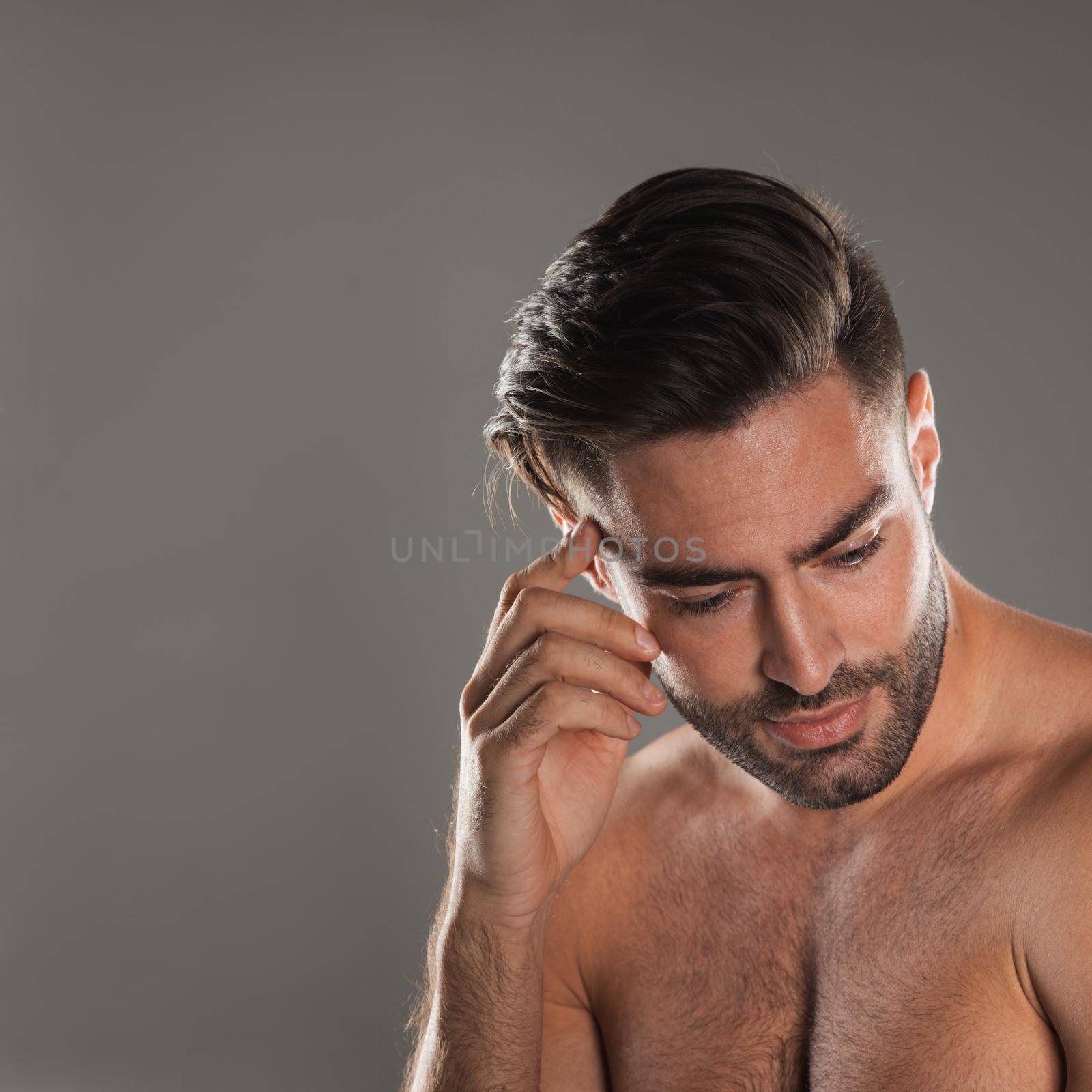 Photo of thoughtful half-naked man posing and looking aside over gray background with copy space