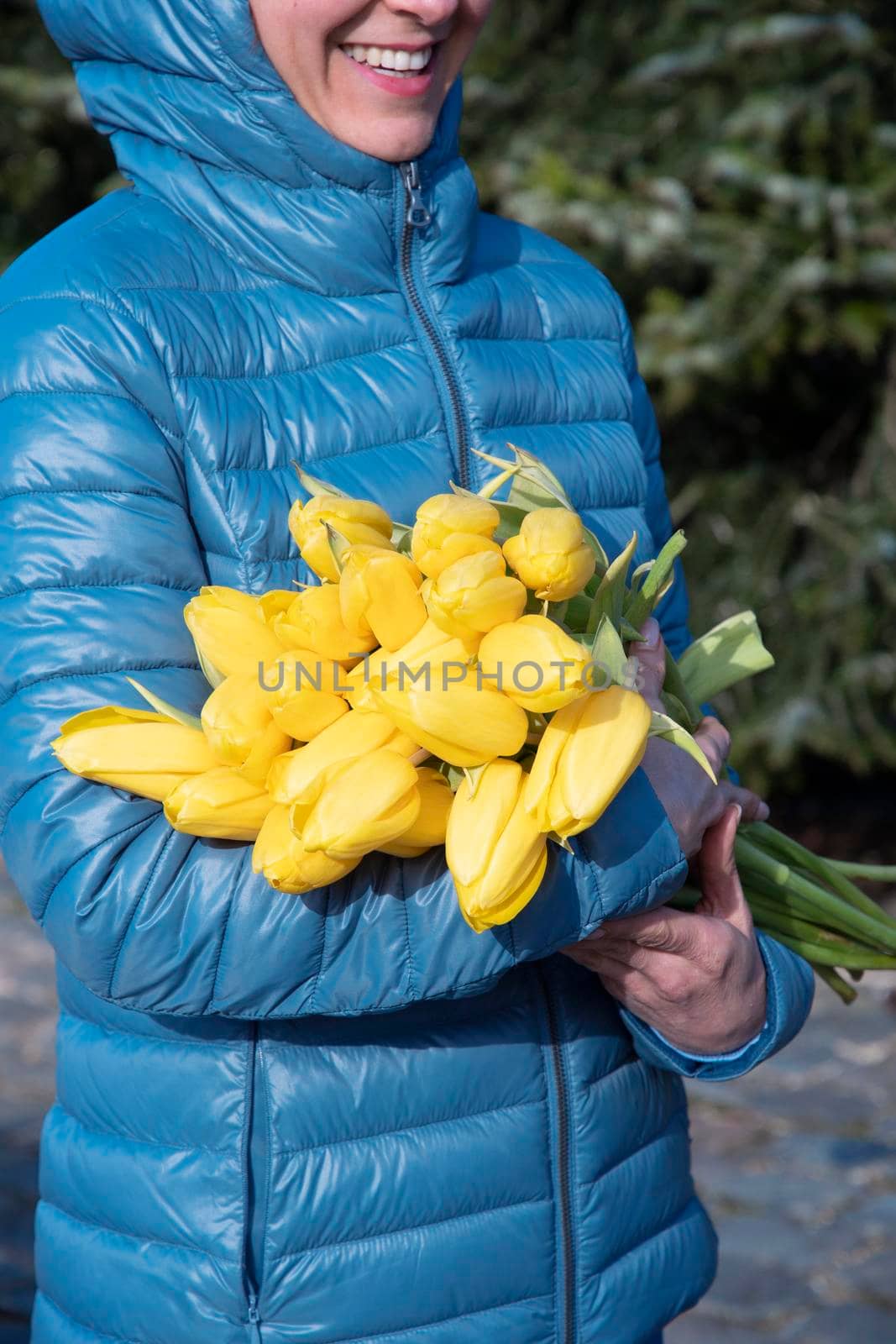woman in a bright blue jacket with a bouquet of yellow spring tulips, mother's day gift. High quality photo