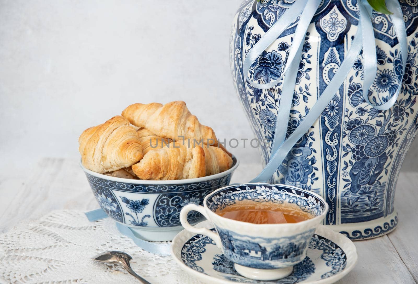 spring still life with croissants and a bouquet of pink luxurious peonies in an ancient Chinese vase with blue ornament, an antique tea cup, early breakfast or brunch, High quality photo
