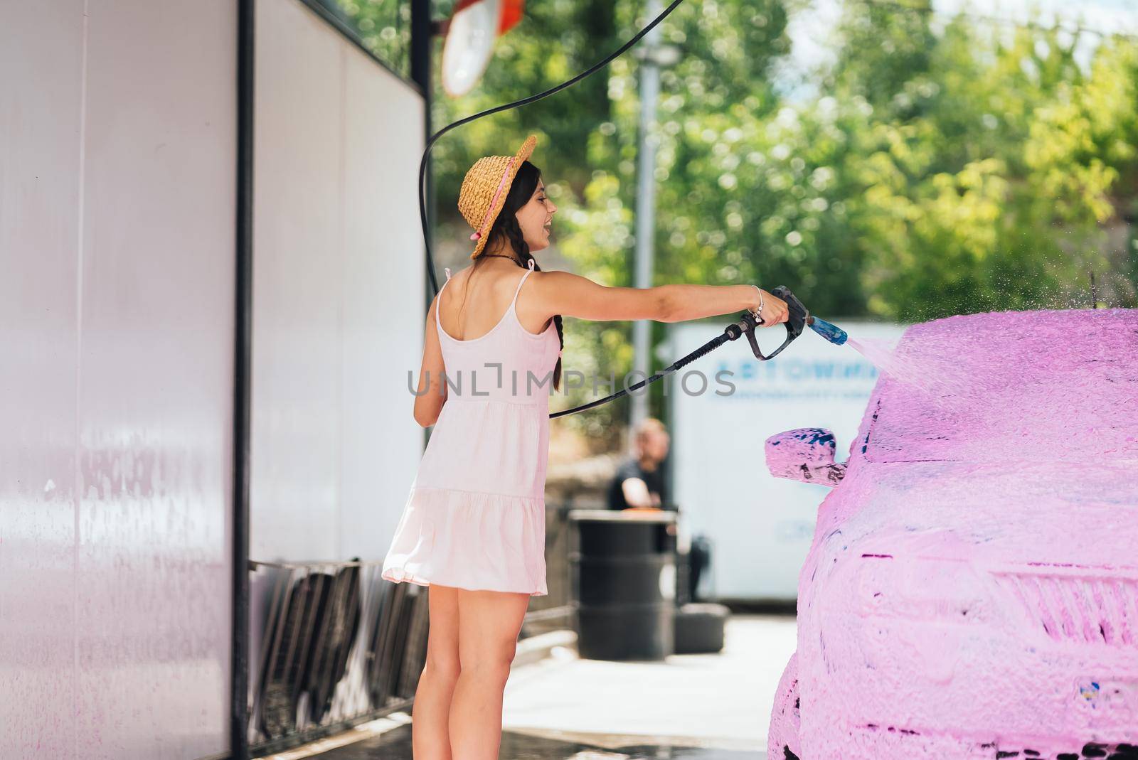 Brunette with long hair from a high-pressure hose applies a cleaner on the car at a car wash