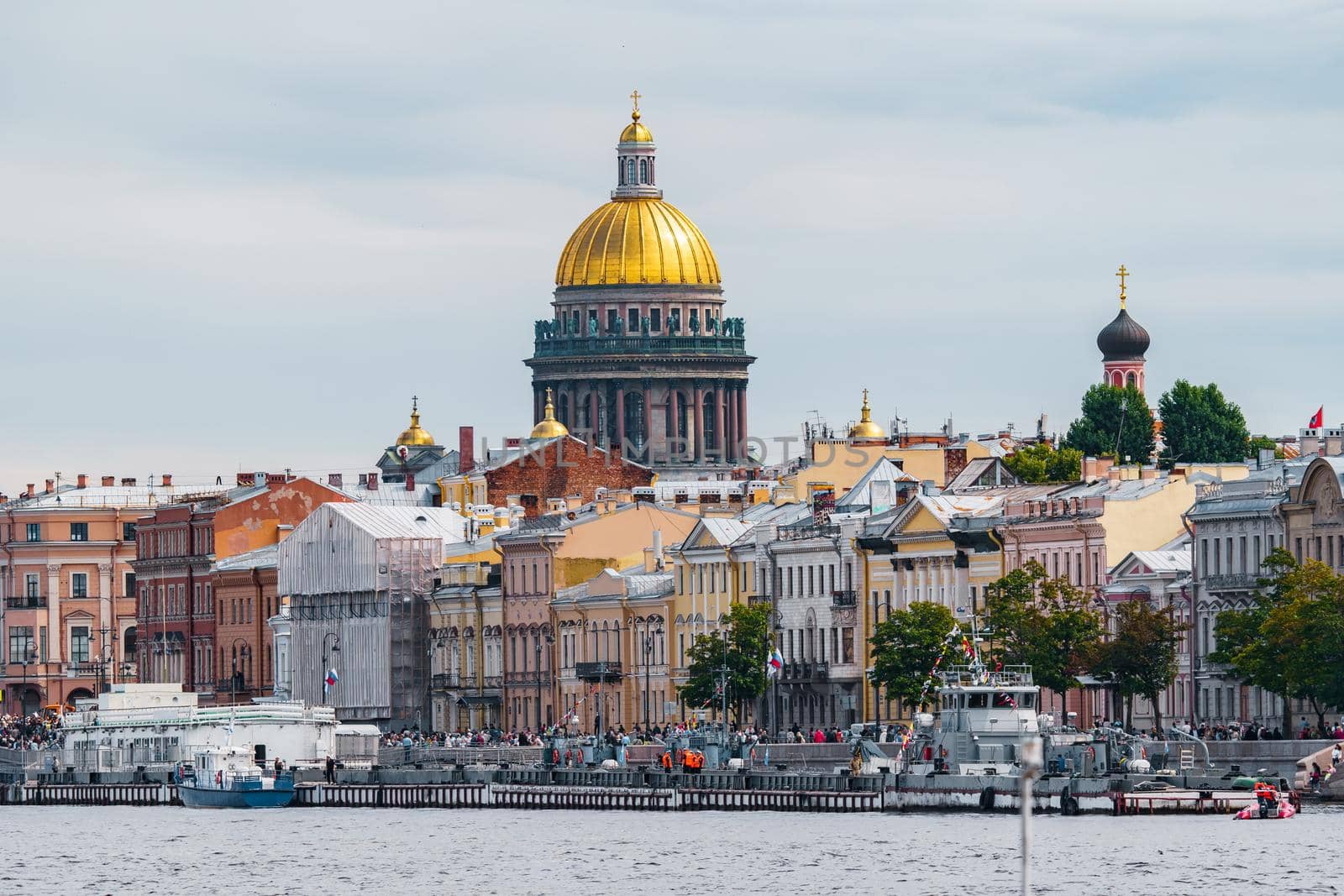The huge golden dome of St. Isaac's Cathedral through the roofs of houses on the embankment of the Neva River in St. Petersburg in cloudy weather. High quality photo