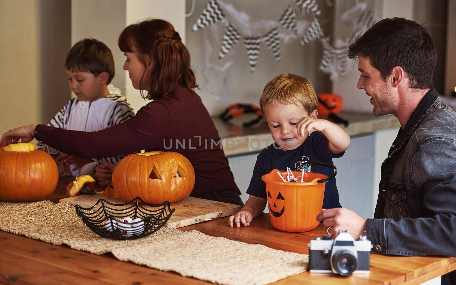 Candy keeps the monsters away on Halloween. an adorable young family carving out pumpkins and celebrating halloween together at home
