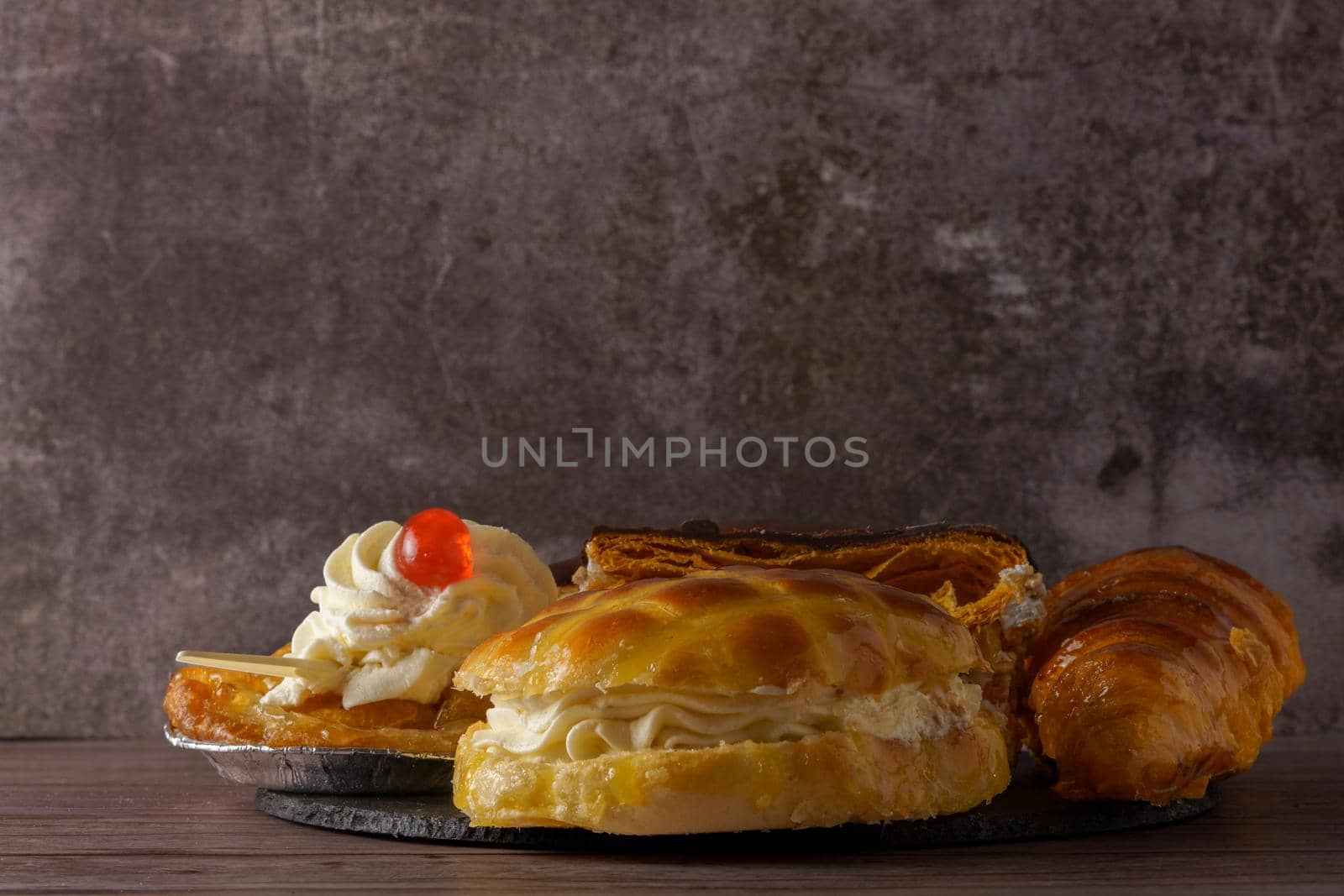 close-up of various types of cakes on a black slate on a wooden table with a gray background