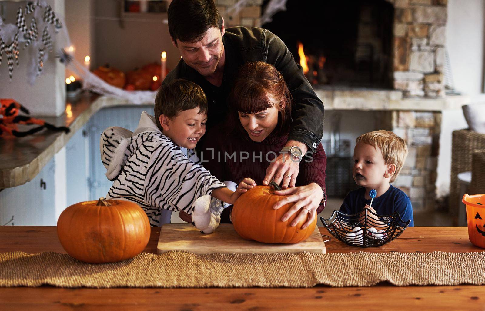 Our family loves celebrating halloween. an adorable young family carving out pumpkins and celebrating halloween together at home. by YuriArcurs