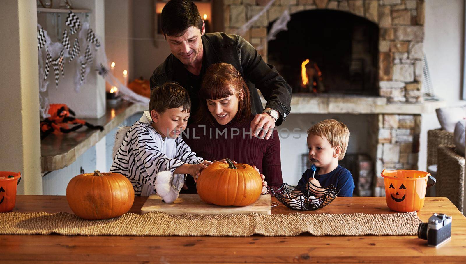 Our family is going to give you the creeps. an adorable young family carving out pumpkins and celebrating halloween together at home. by YuriArcurs