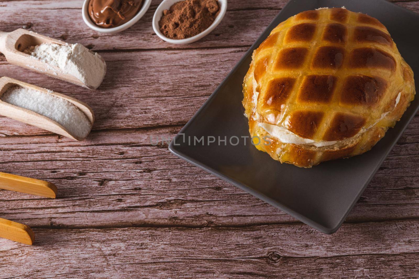 cream-filled bun covered with sugar syrup on a blue plate on a wooden table with spoons with its toppings
