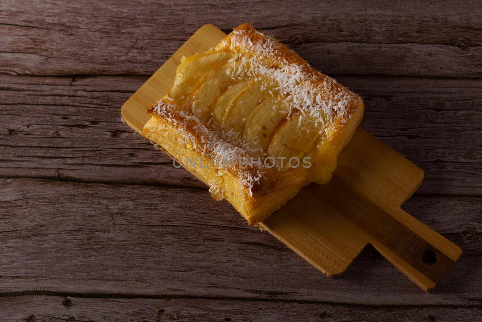 apple tartlet topped with syrup and shredded coconut, on a wooden board