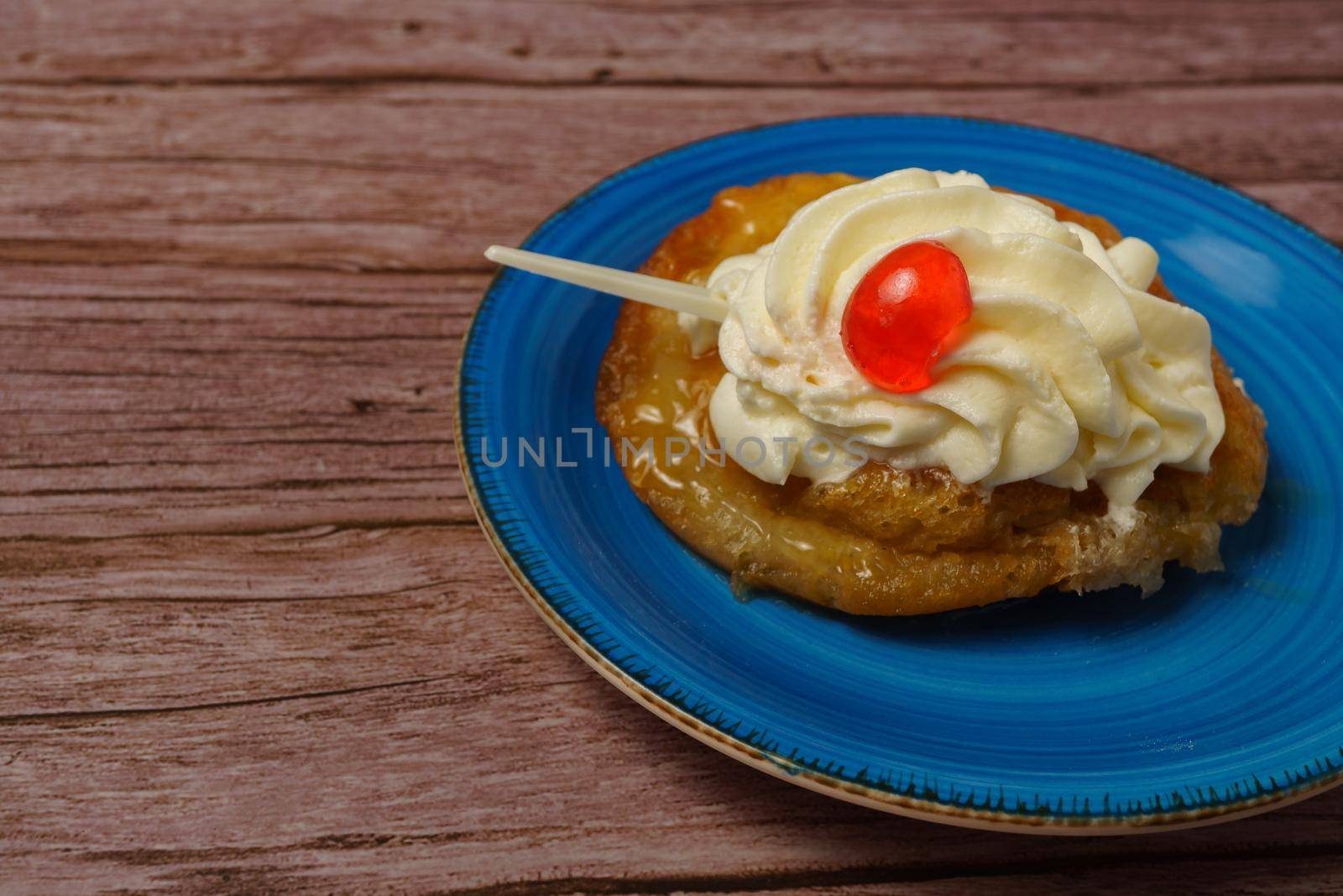 puff pastry dough cake with liqueur and cream, a cherry on top and spoon on a wooden table