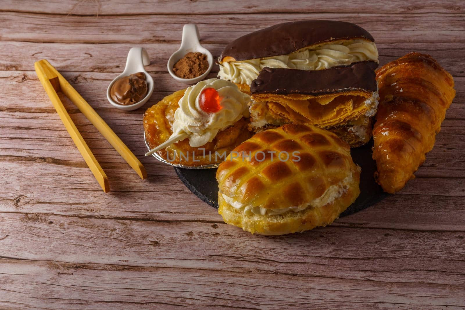 close-up of various types of cakes on a black board with ceramic spoons and wooden tongs on a wooden table