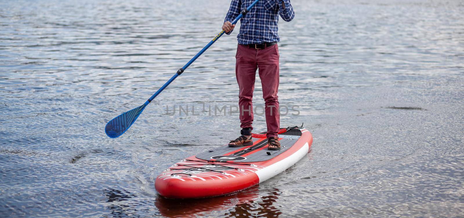 SUP board Stand up paddle man boarding on lake standing happy on blue water. A man swims and rests on a SUP board on the river