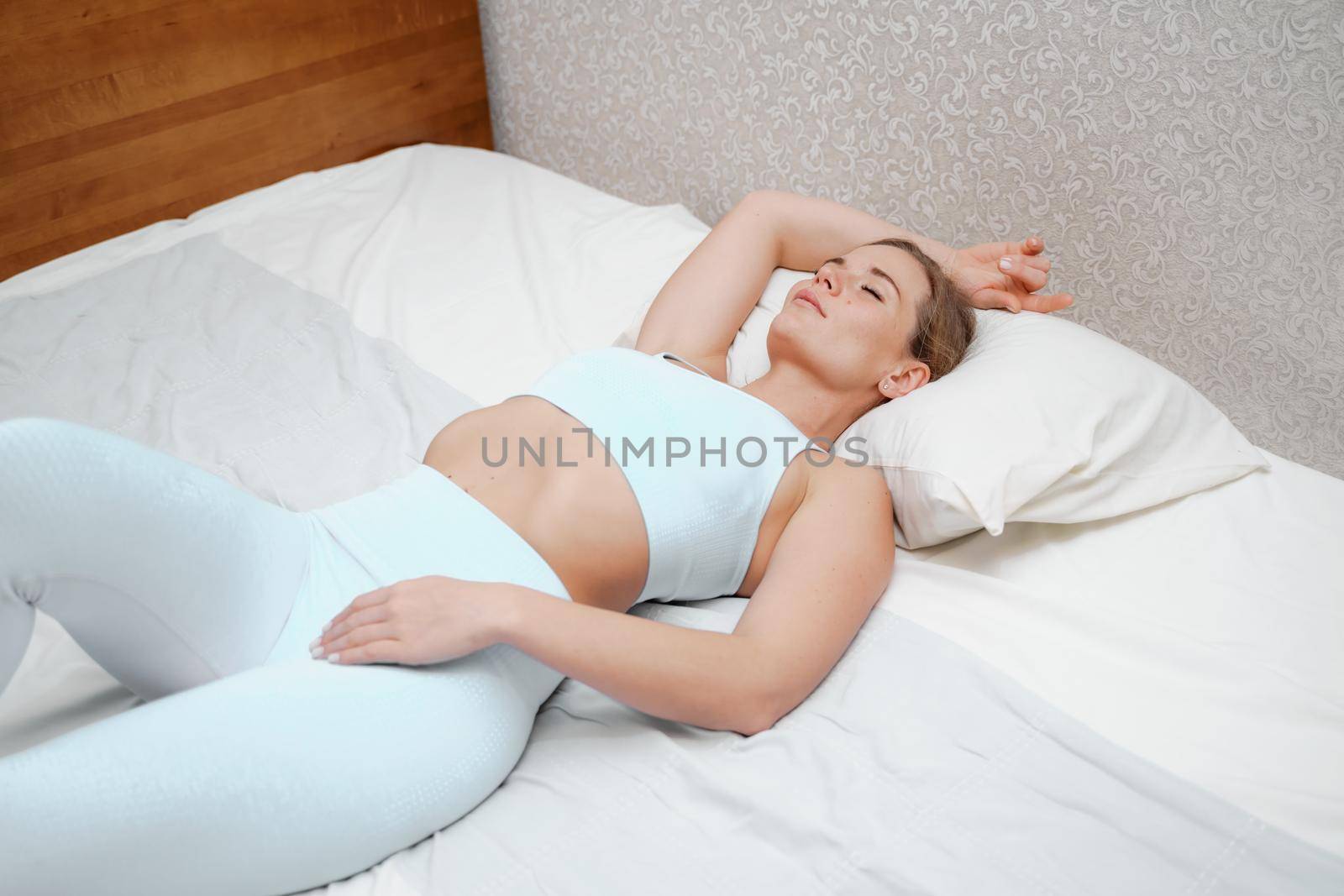 A young woman lies on a bed without a blanket. Bed linen is white