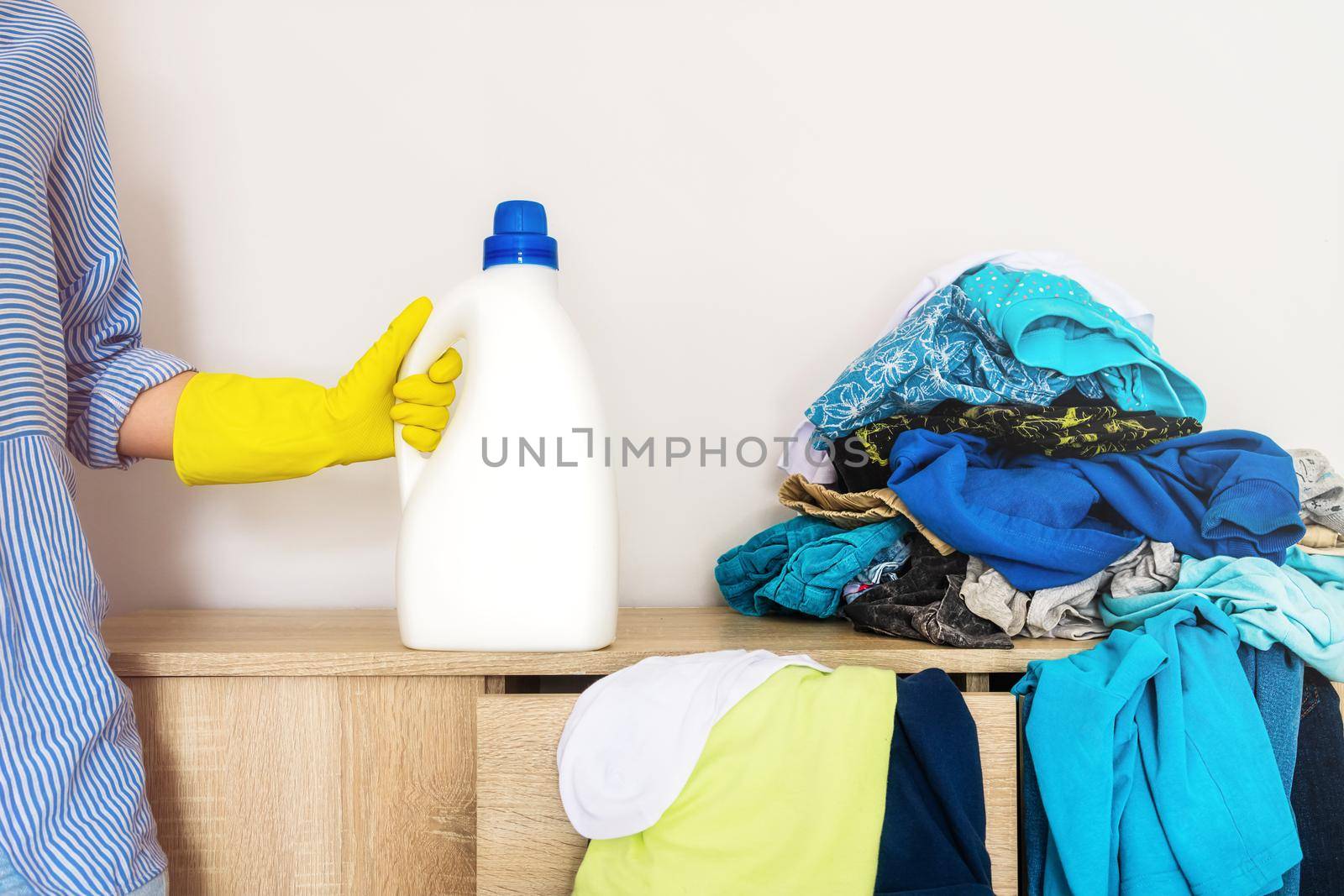 Close-up of a female hand in a yellow rubber glove holding a bottle of liquid laundry detergent. Label mockup, logo for cleaning, bleaching, house cleaning. mess, hygiene concept, space organization
