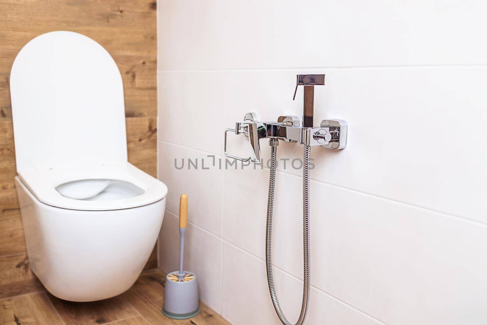 Fashionable bathroom in a minimalist style interior. Close-up of a white toilet bowl and a chrome-plated hygienic shower on the wall. The concept of hygiene, body care. Modern sanitary equipment