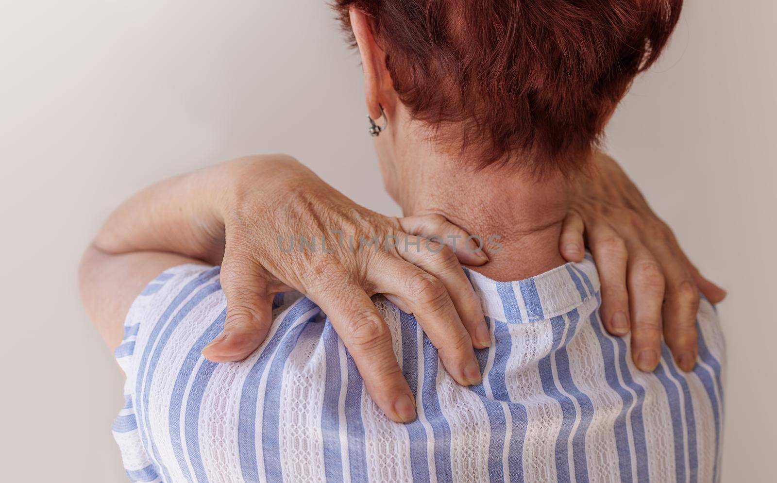 Close-up massage technique, neck and collar zone. Spinal problems and neurological diseases in the elderly. Hands of an old man doing massage on his own. A woman in a blue shirt stands with her back
