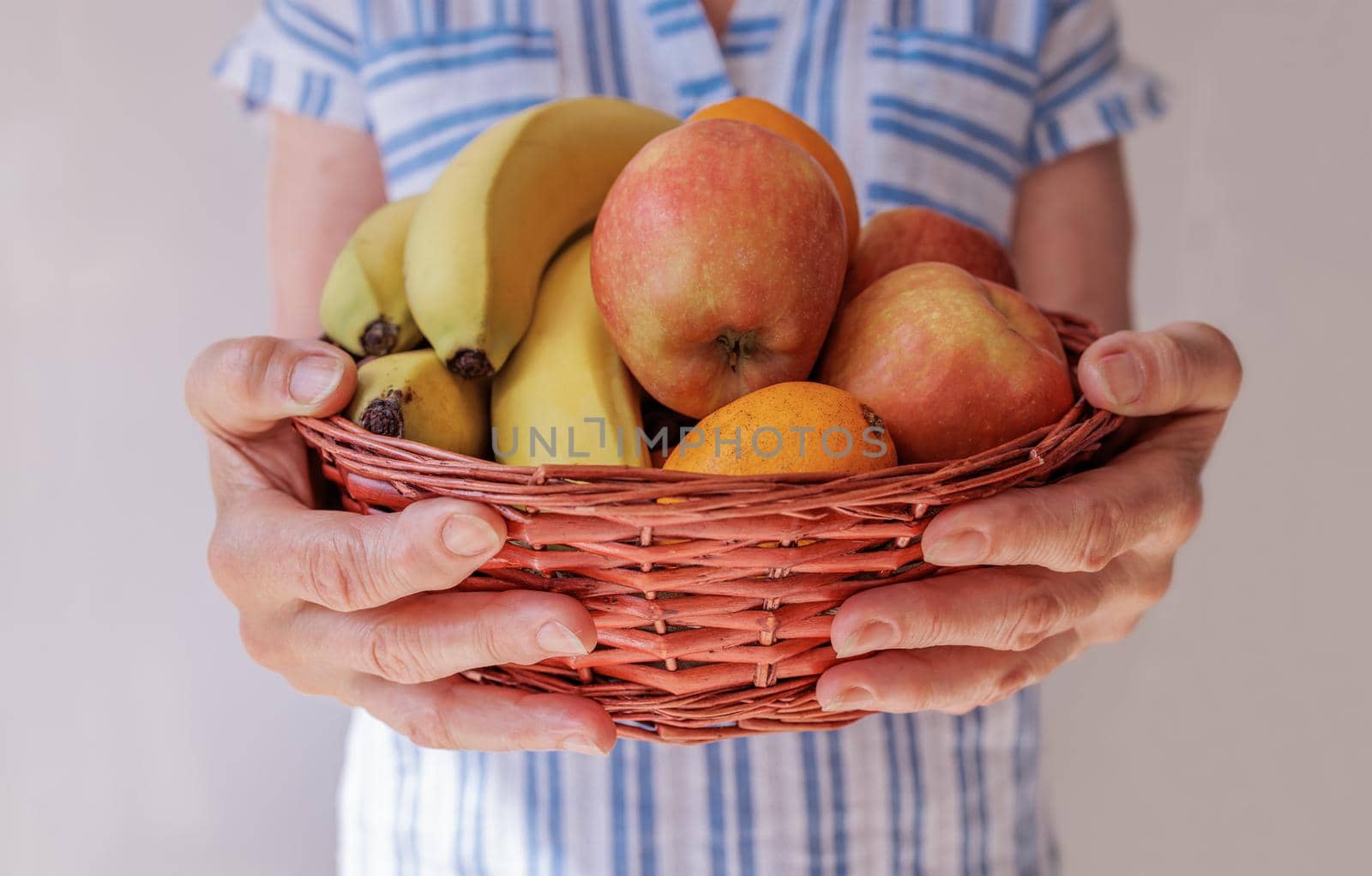 close-up, the hands of an elderly woman hold a basket of healthy fruits by Ramanouskaya
