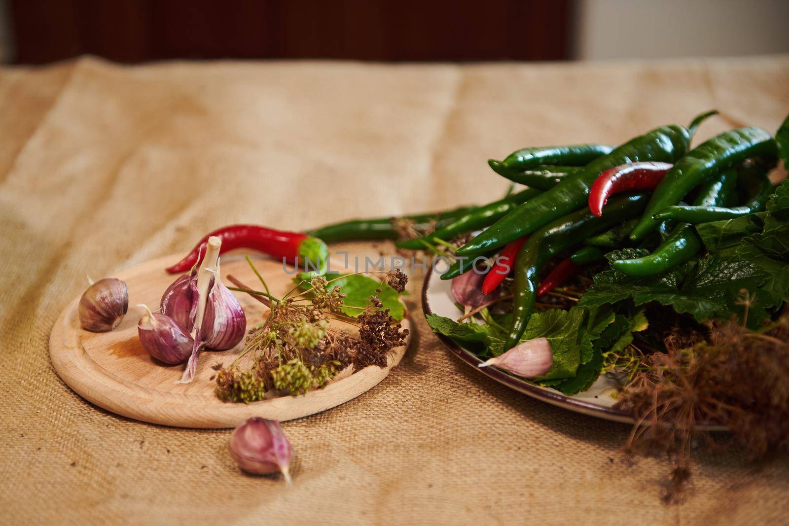 Still life with fragrant culinary herbs and ingredients for preparing brine, marinade and pickle: garlic cloves, fresh dill leaves and chili peppers on wooden board on a table with a linen tablecloth