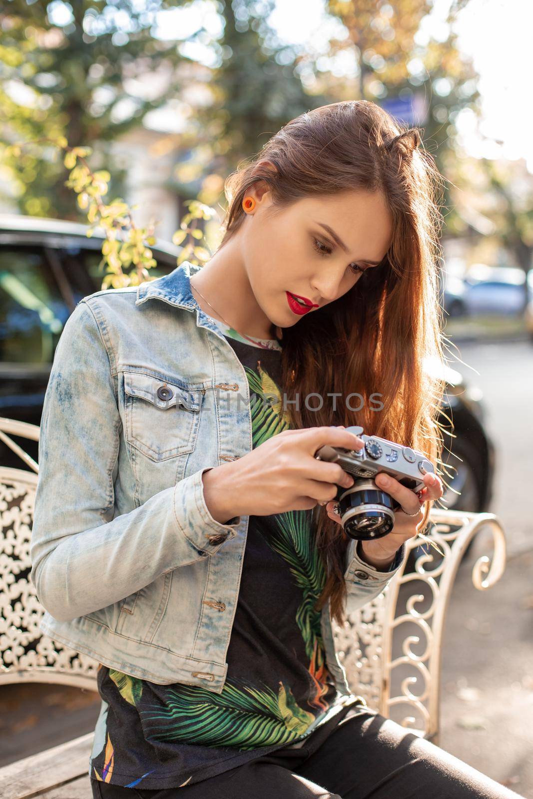 Happy hipster girl making photo with retro camera on city street. Travel concept