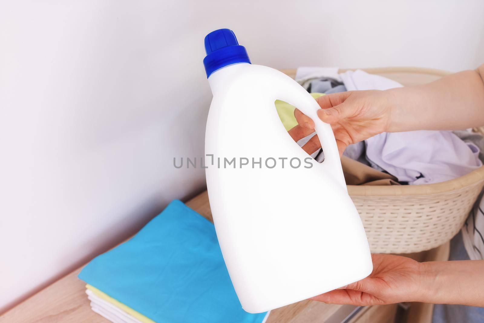 Close-up, in the hands of a woman is a large white bottle, a template for a label, logo. Liquid detergent, fabric softener, bleach, laundry detergent. copy paste white background