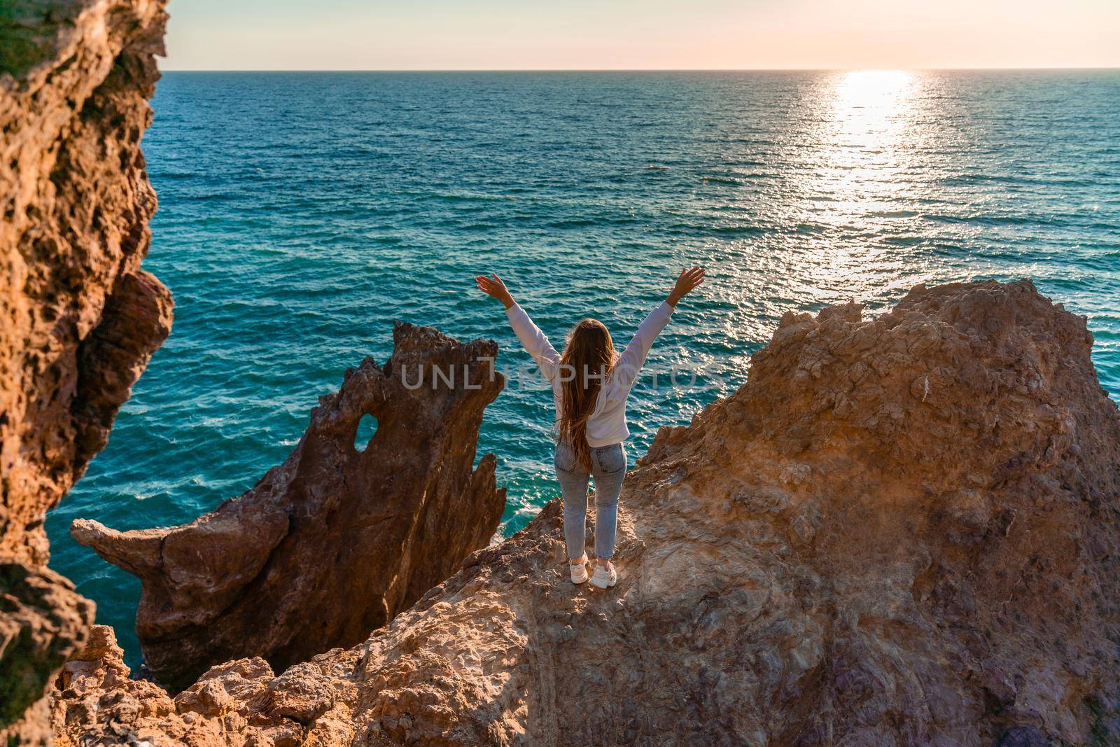 A female tourist, standing with her hands up, reaches the ends of the earth and sees the dragon rock. The girl welcomes the sun. Concept design. A successful woman looks at the sunset with open arms. by Matiunina