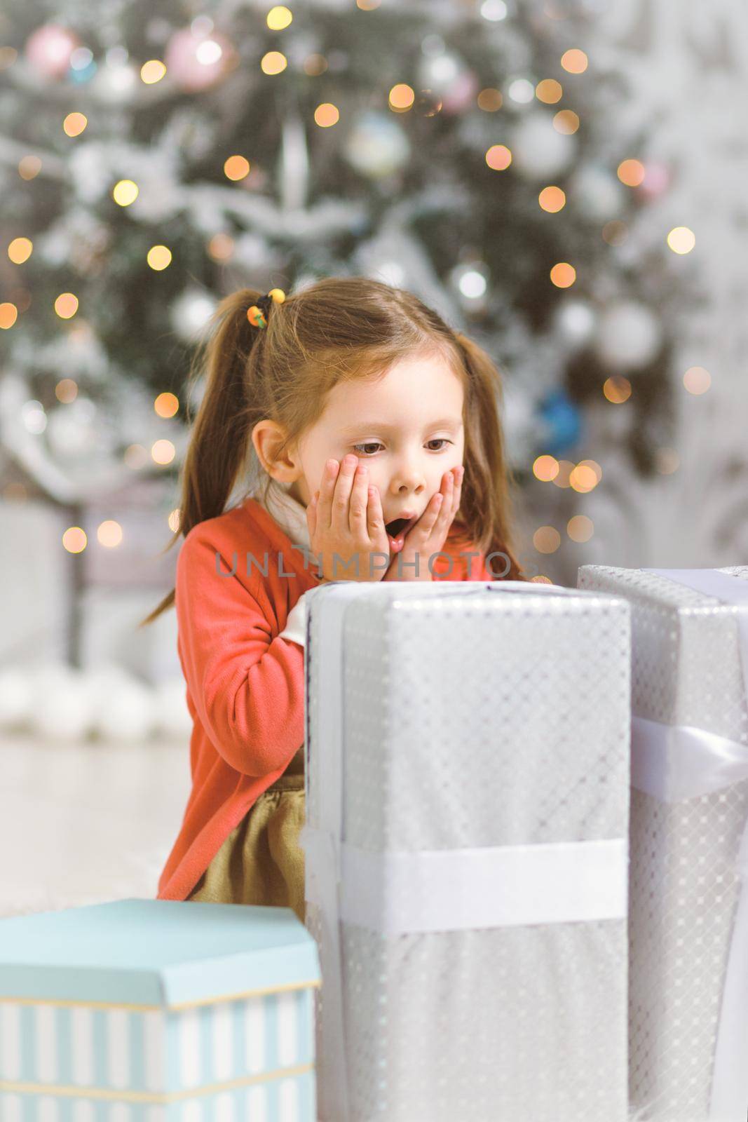 Emotional little girl with New Year gifts in white interior with christmas tree by Rom4ek