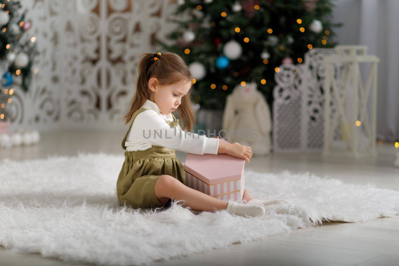Cute kid girl holding new year gift while sitting on the white carpet.