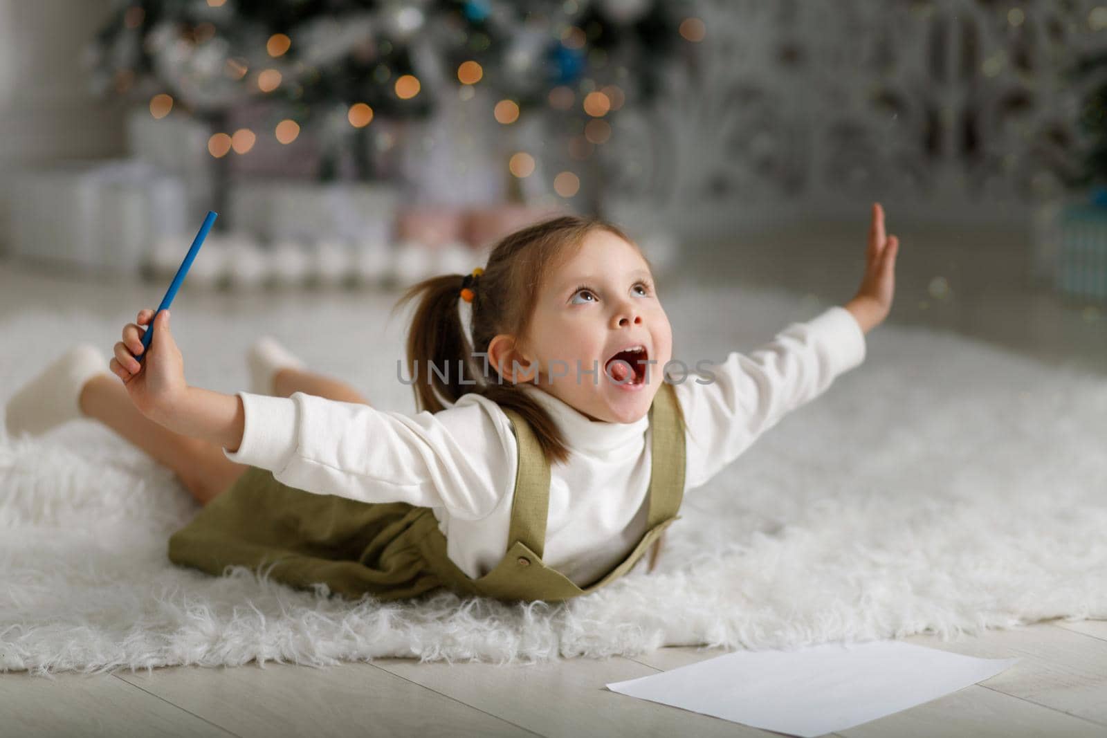 Little girl fooling around on the floor and writing a letter to santa claus.