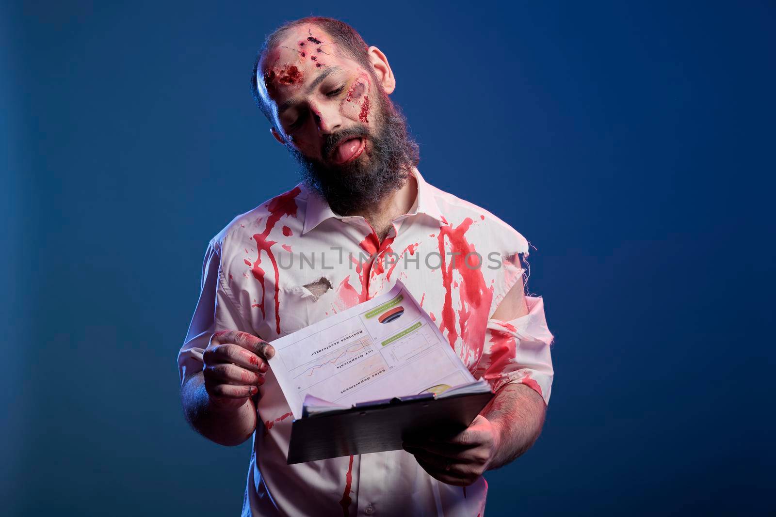 Spooky halloween monster looking at business documents, analyzing paperwork notes in front of studio camera. Undead horror zombie holding papers, being scary and dangerous brain eating corpse.