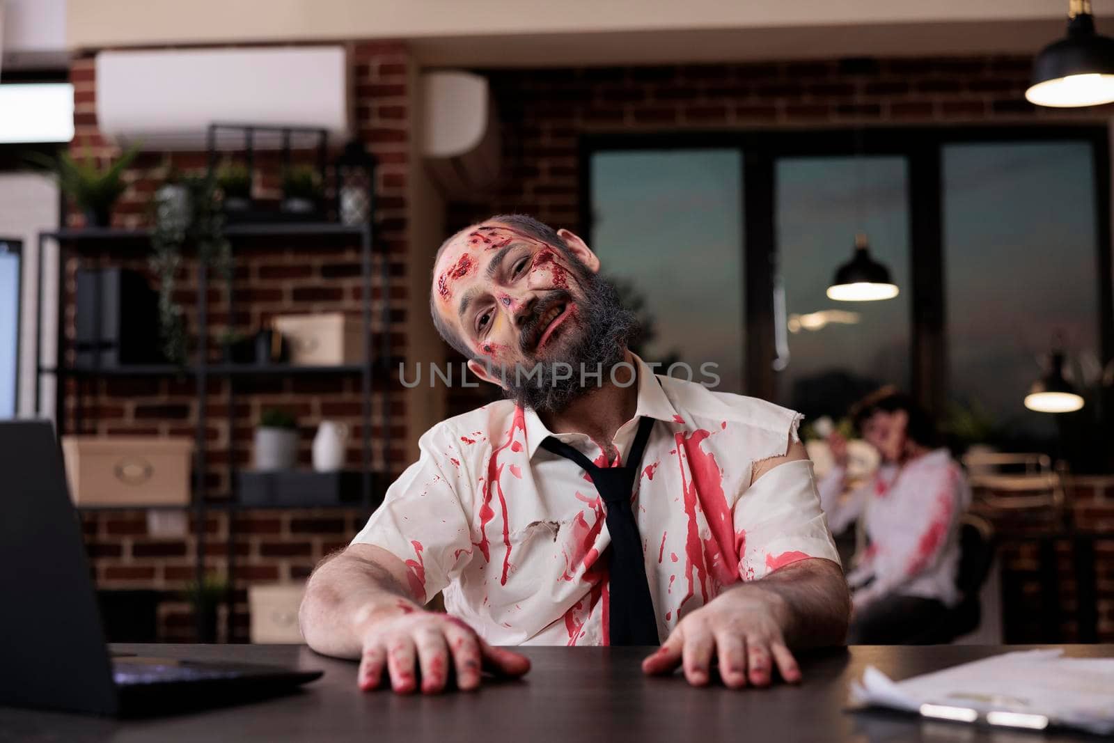 Portrait of walking dead corpse in office working on startup business with laptop, creepy evil monster sitting at desk. Brain eating horrific zombie with bloody wounds and dirty scars, eerie walker.