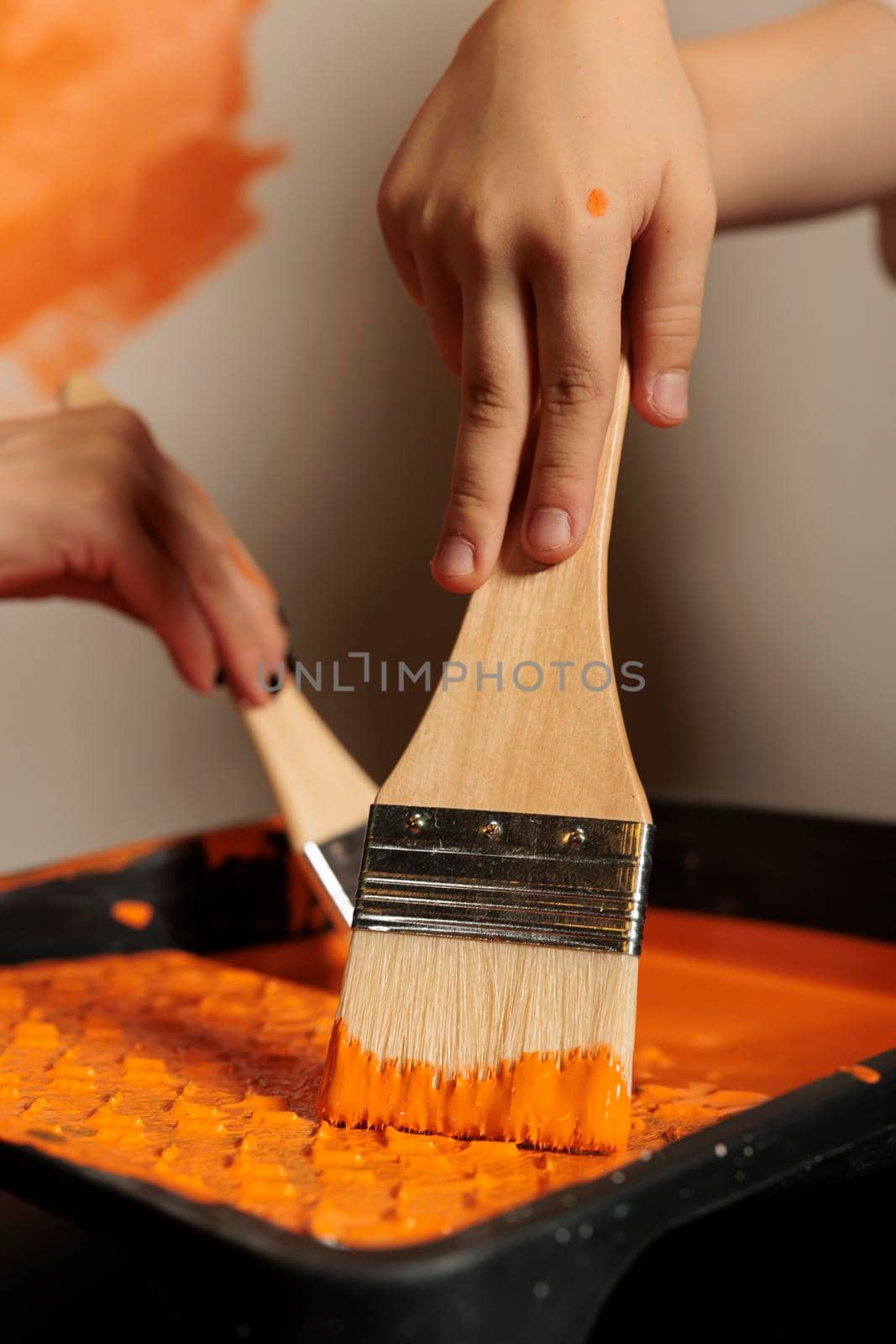 Small family using paintbrush and color to paint room walls, holding brush with bristles in liquid acrylic can. People painting apartment with paintwork tools, surface design renewal. Close up.