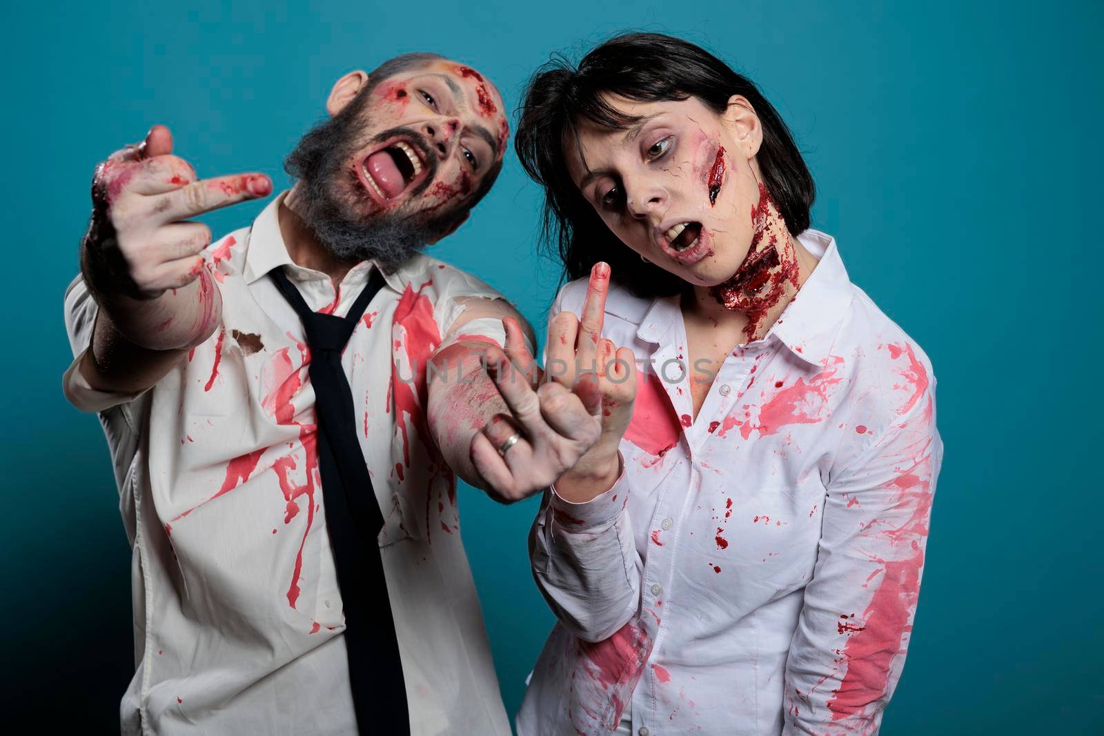 Aggressive halloween zombies showing middle finger on camera, acting vulgar and rude with mean gesture. Dangerouns creepy evil monsters with bloody wounds looking deadly and frightening.