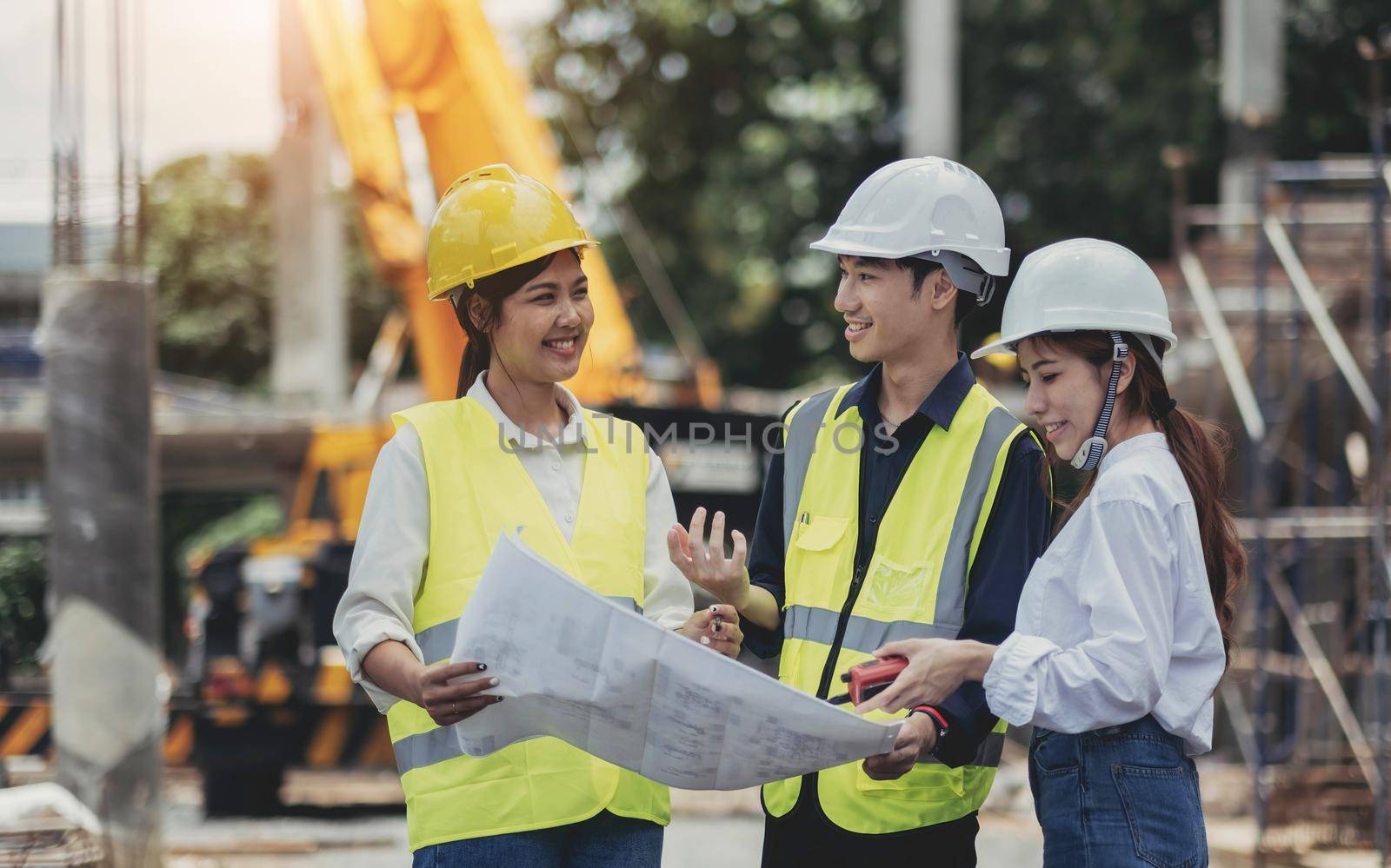 Three experts inspect commercial building construction sites and construction site holding blueprints.