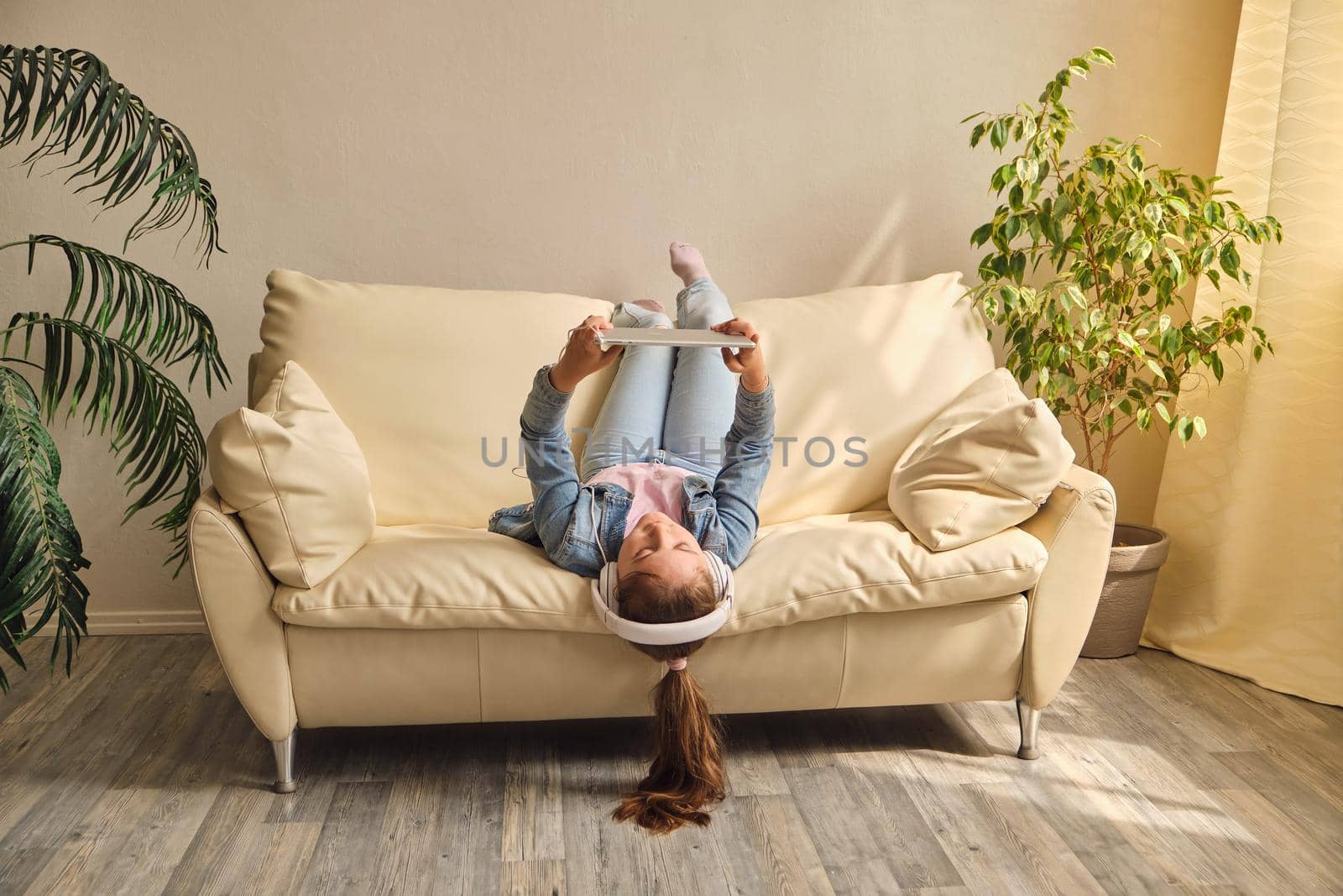 little girl lying upside down on sofa and play with tablet
