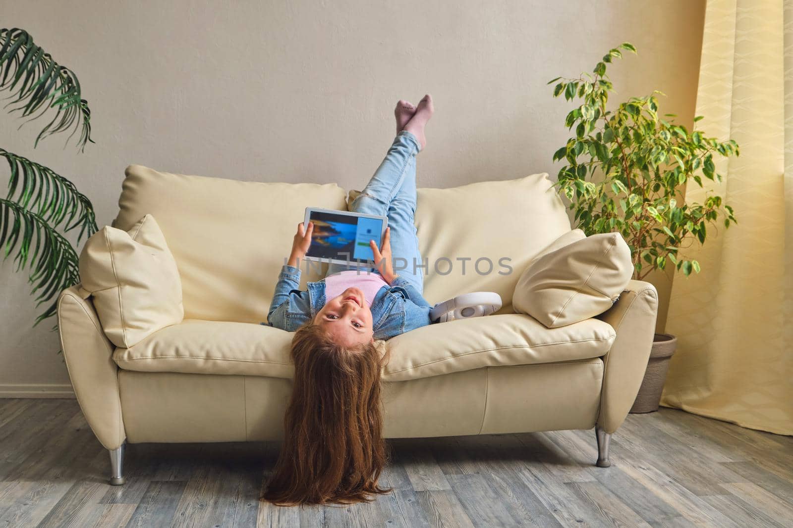 little girl lying upside down on sofa and play with tablet
