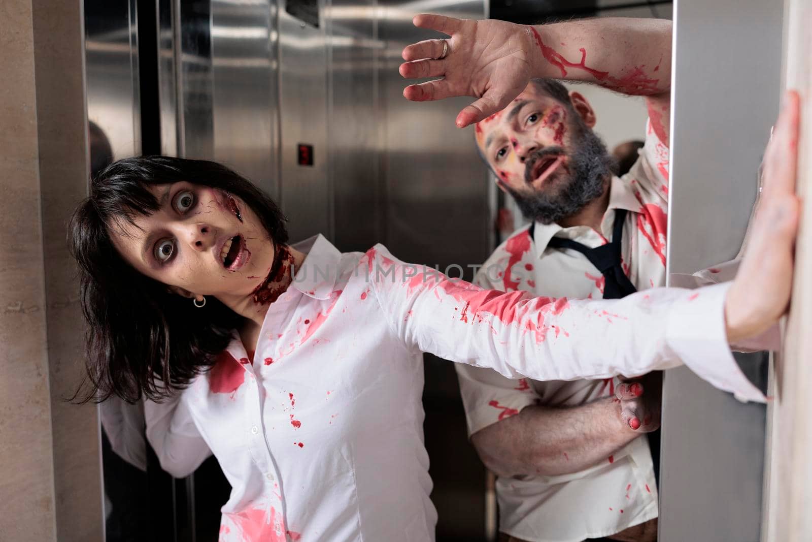 Portrait of zombies couple in office elevator, escaping to chase after people and looking scary terrifying. Brain eating corpses with scars attacking workplace, horrific aggressive walking dead.