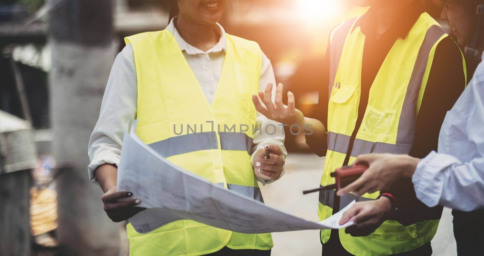 Three experts inspect commercial building construction sites and construction site holding blueprints.