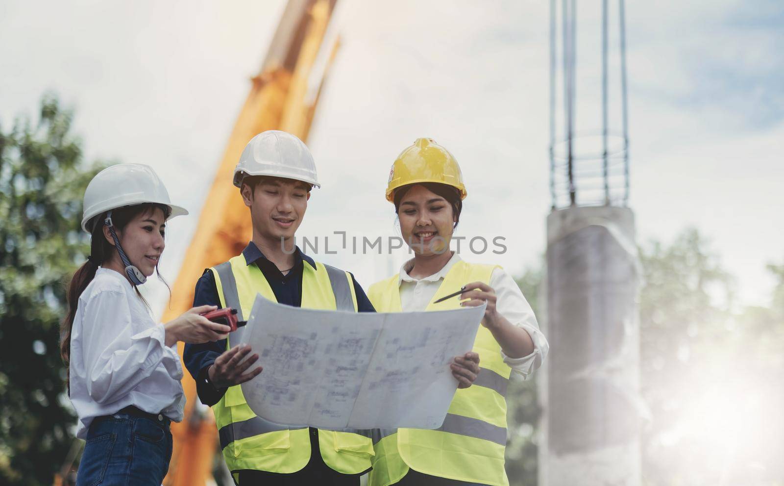 Three experts inspect commercial building construction sites and construction site holding blueprints by wichayada