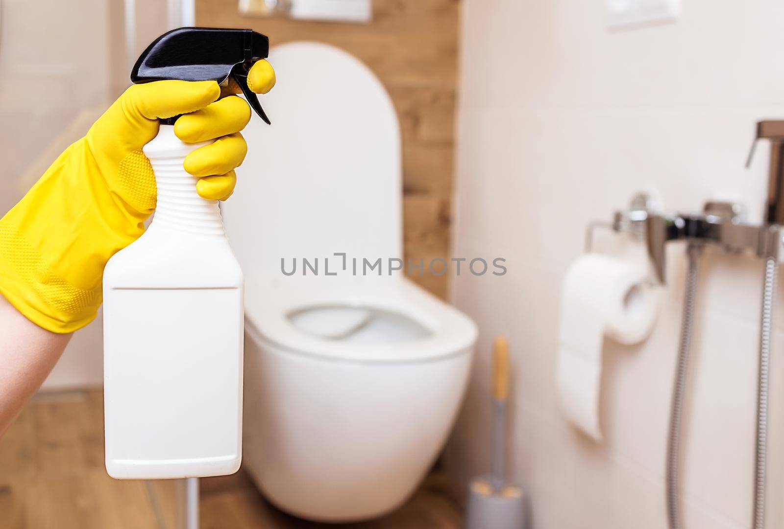 close-up, a woman's hand in a yellow rubber cleaning glove holds a white bottle with liquid cleaner. Mockup for sanitary, hygienic cleaning liquid. Copy paste space for label, logo, trademark, design