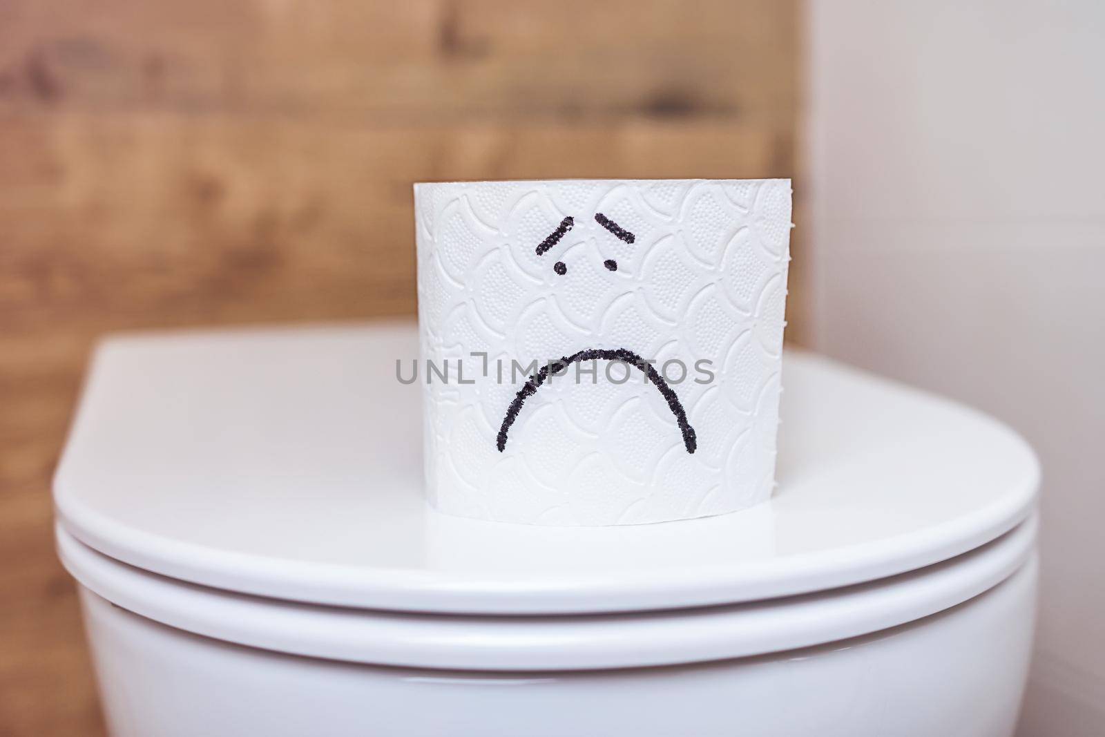 close-up roll of white toilet paper with a painted sad face stands on the toilet. The concept of bad mood, health problems, constipation, hemorrhoids, intestinal problems. Personal hygiene, self care