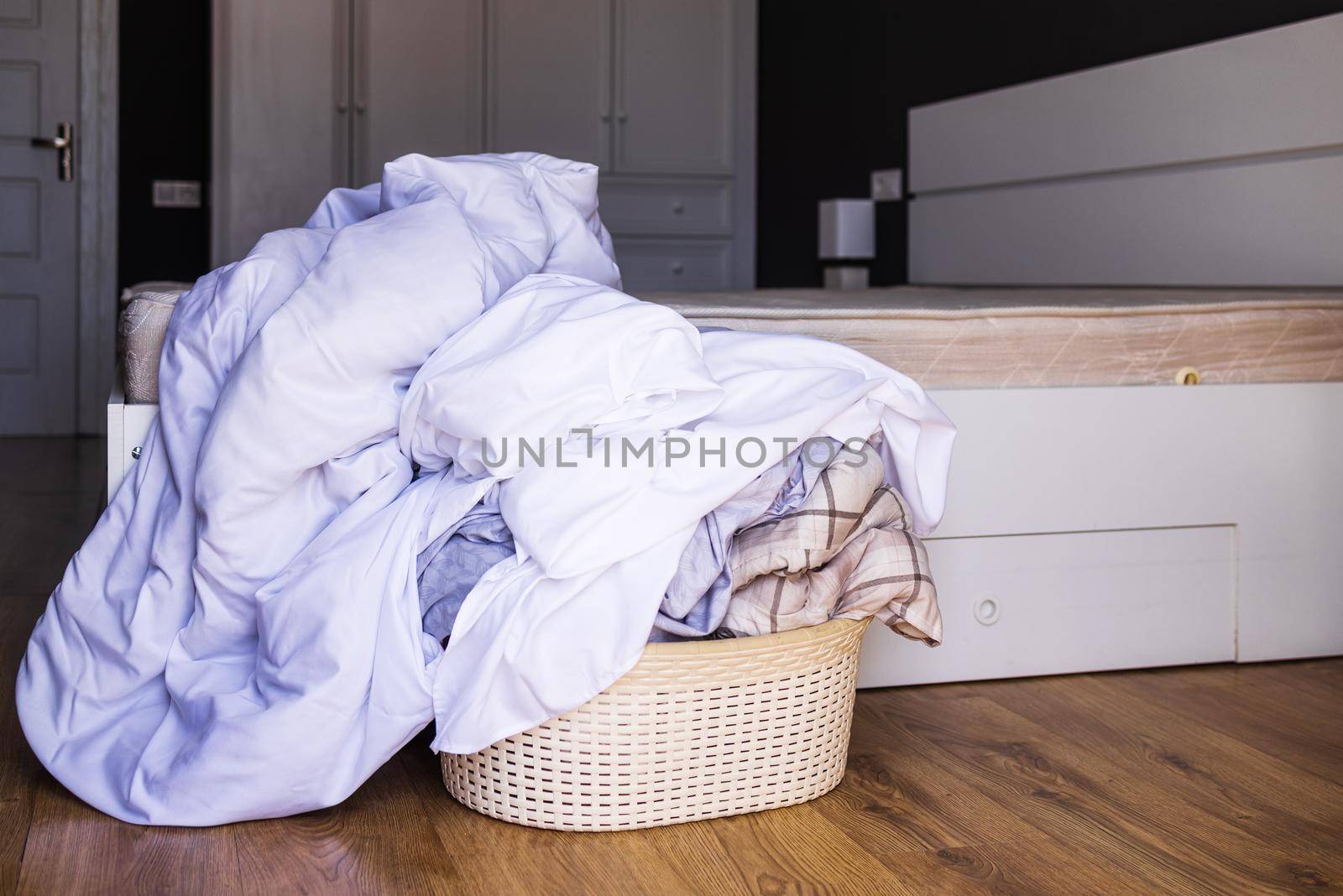 Close-up of a large pile of white bed linen gathered in a basin that stands next to a large bed in a hotel room. Laundry laundry concept, hotel room cleaning service