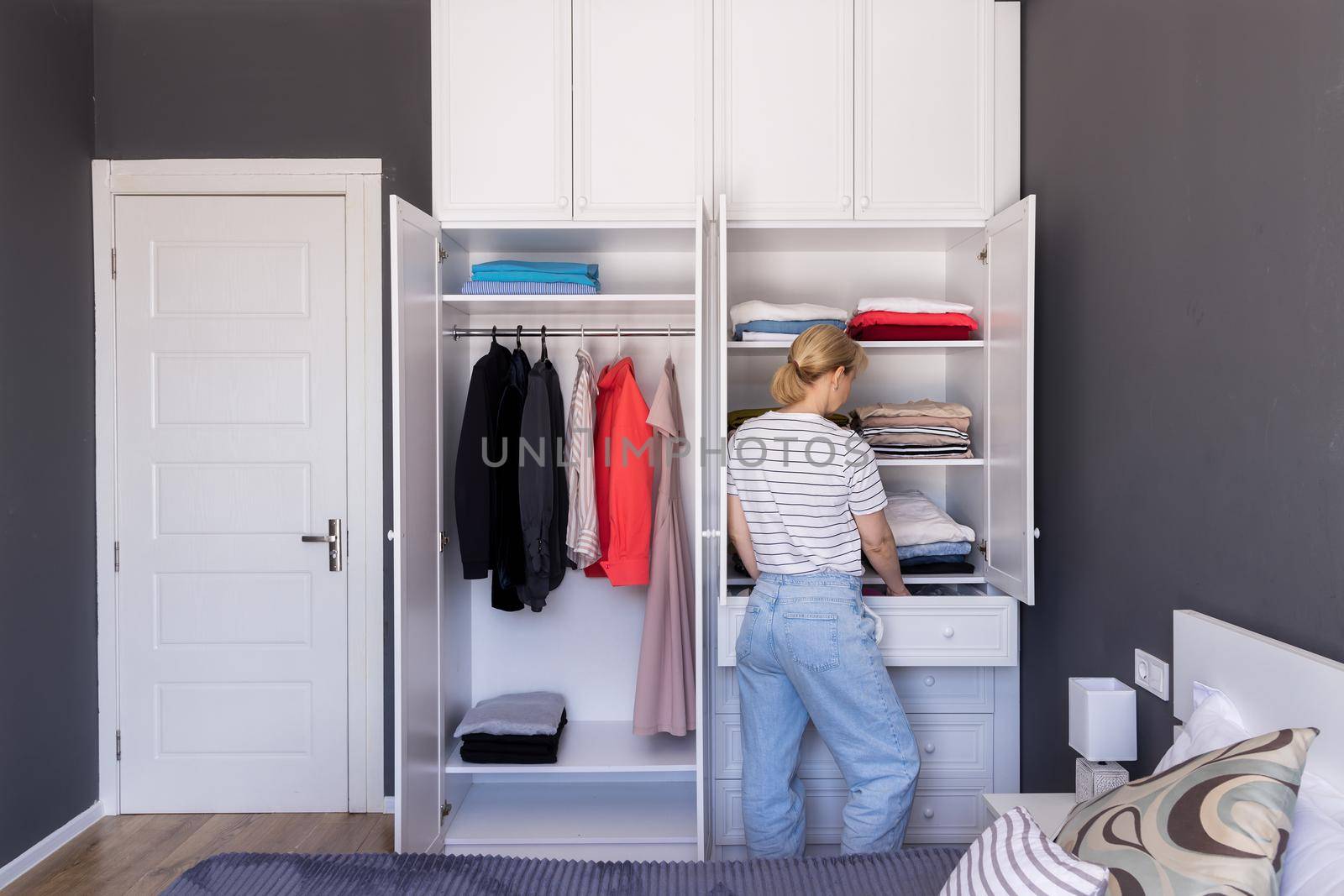 girl stands near the closet, puts things in order on the shelves with underwear by Ramanouskaya