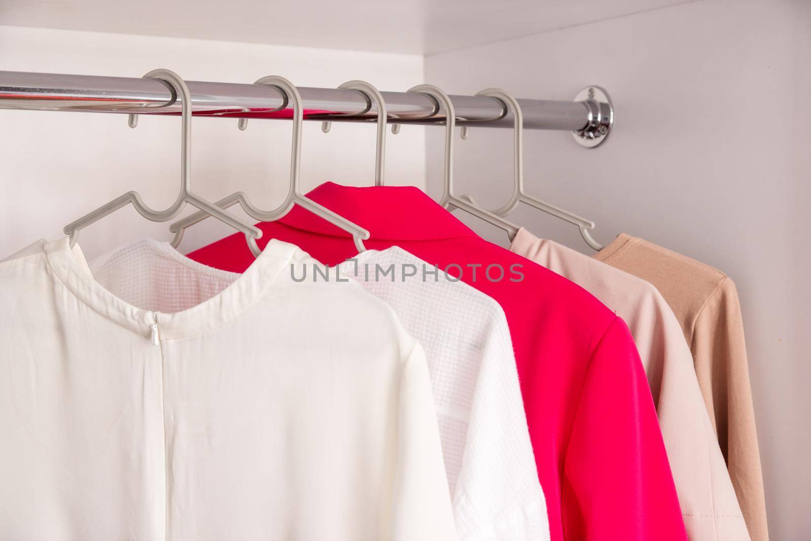 The basic wardrobe of a fashion stylist. Neutral colors: white, black, beige and accent French red. White wardrobe, gray hangers. Minimalism style