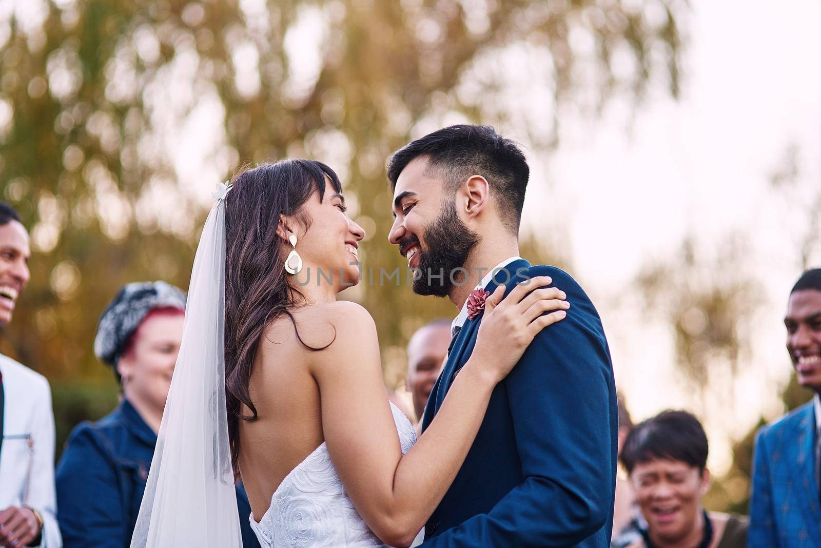 Sharing a moment called happy. an affectionate young newlywed couple smiling at each other on their wedding day with their guests in the background