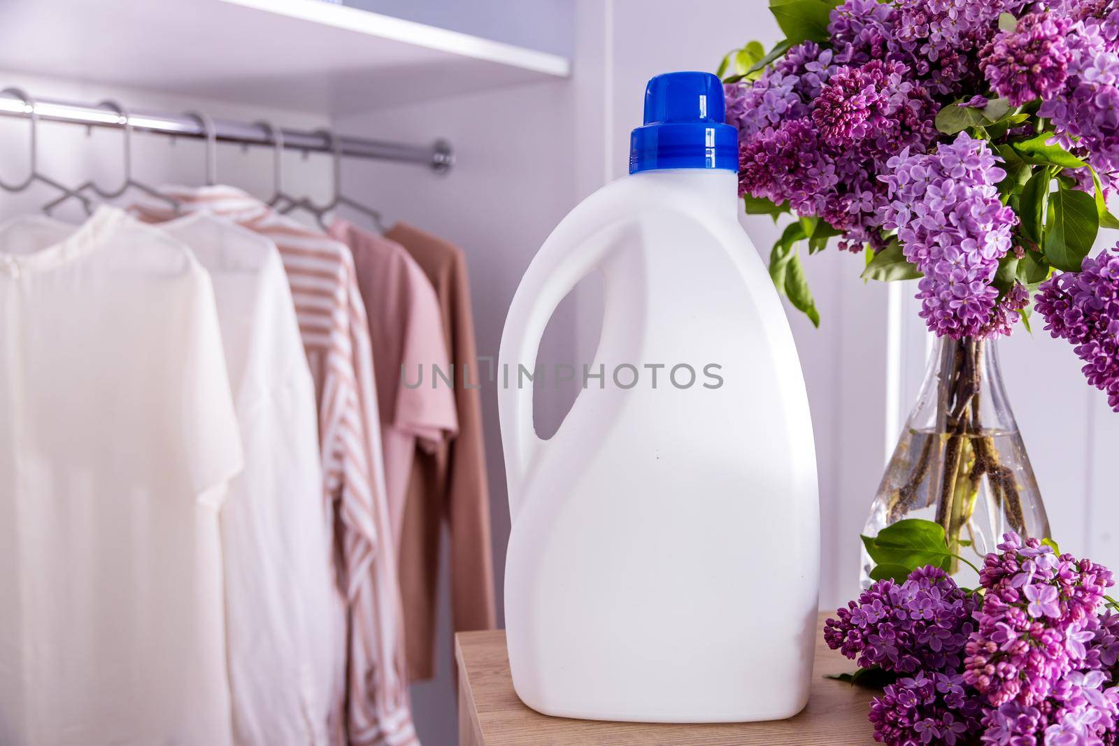 Eco design Mockup of empty bottles packaging laundry detergent against a closet with clothes in neutral tones. Place for text. Bio organic product. Nearby stands a bouquet of lilacs in a vase