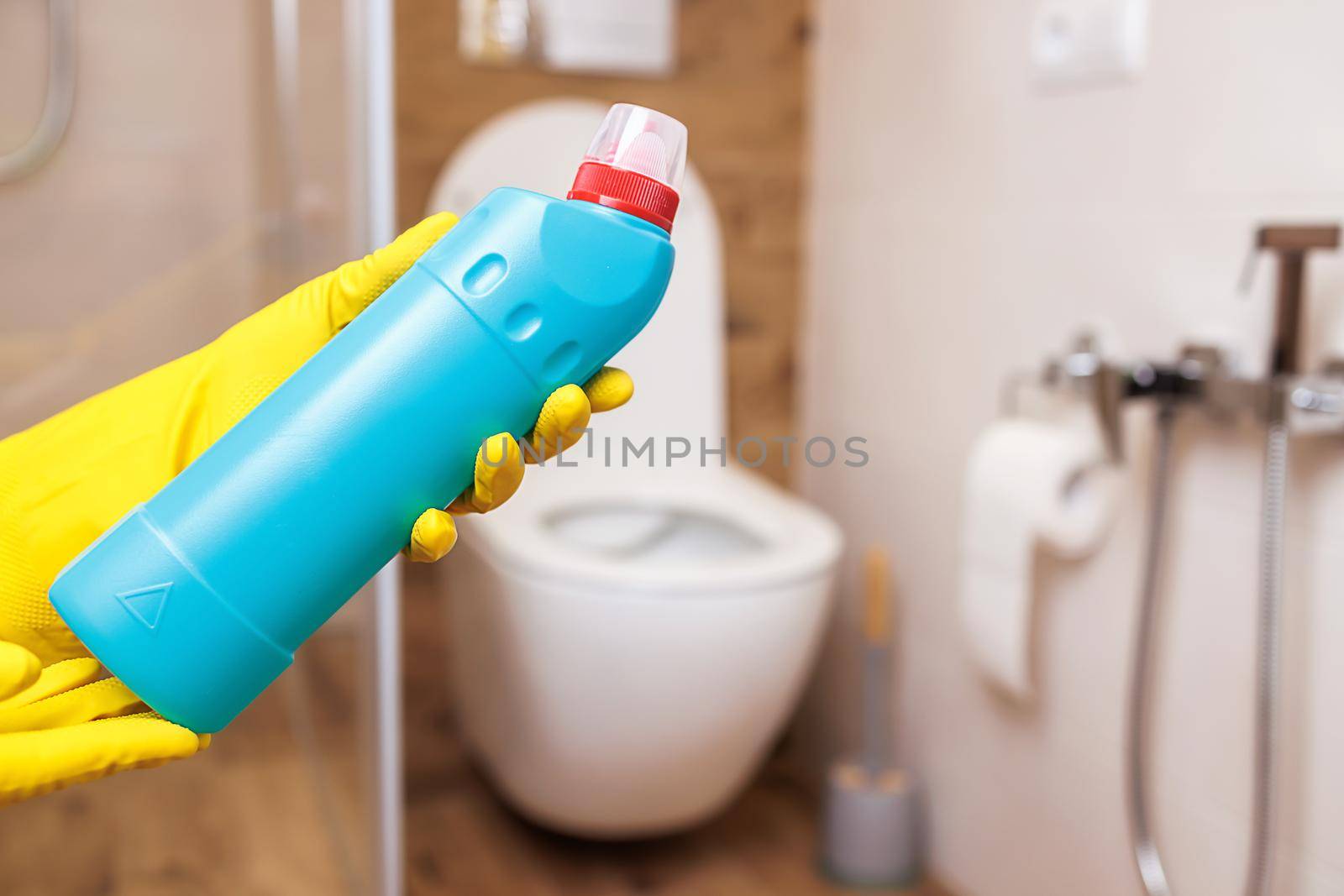 close-up, two hands in yellow rubber gloves for cleaning, hold a blue bottle with liquid cleaner. Mockup for sanitary, hygienic cleaning liquid. Copy space to paste label, logo, trademark, design.