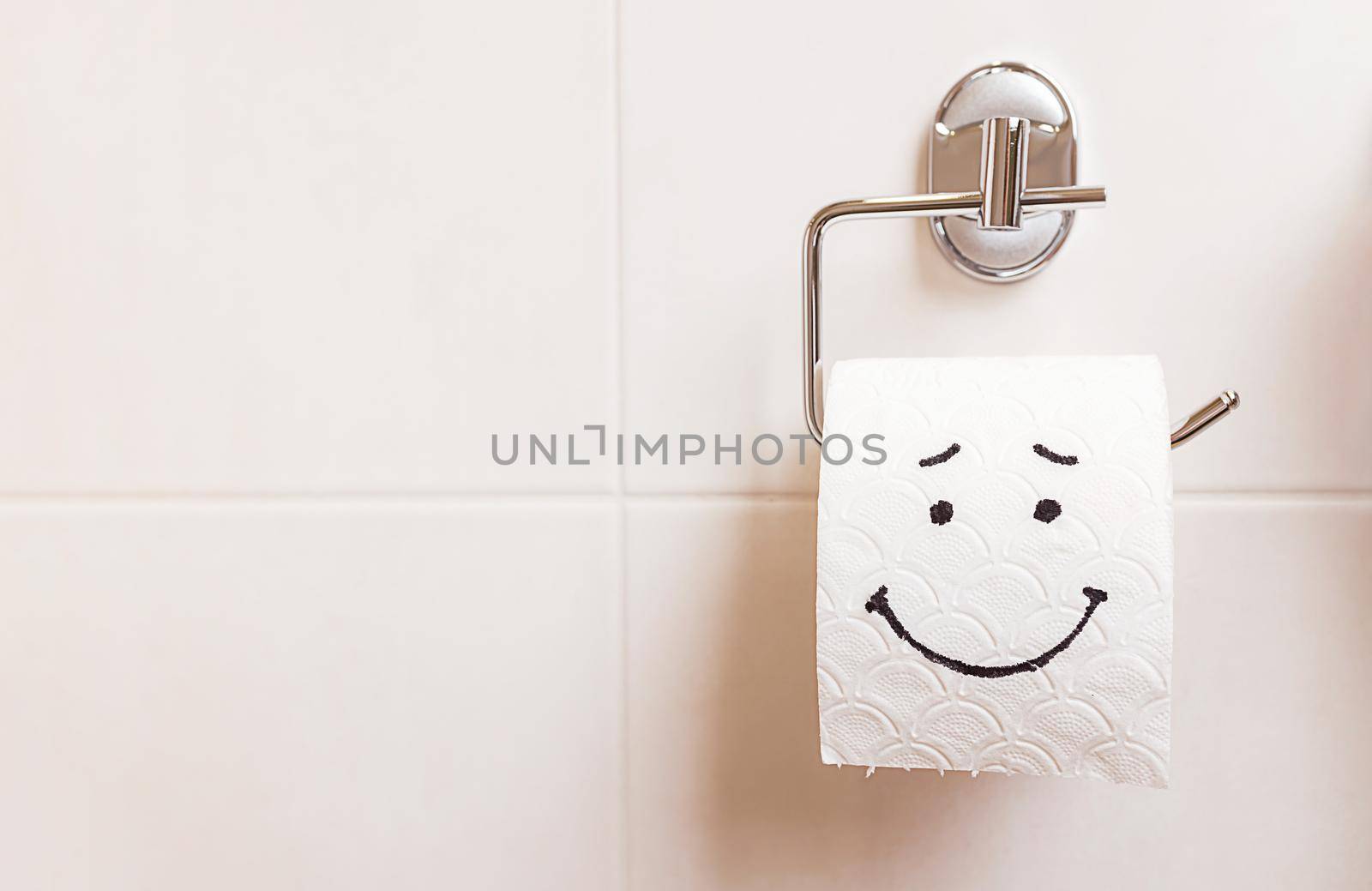 Close-up of a toilet paper roll with a funny emoji hanging on the bathroom wall. The concept of good health, clean bathroom, happy life. Copy paste for your design and text