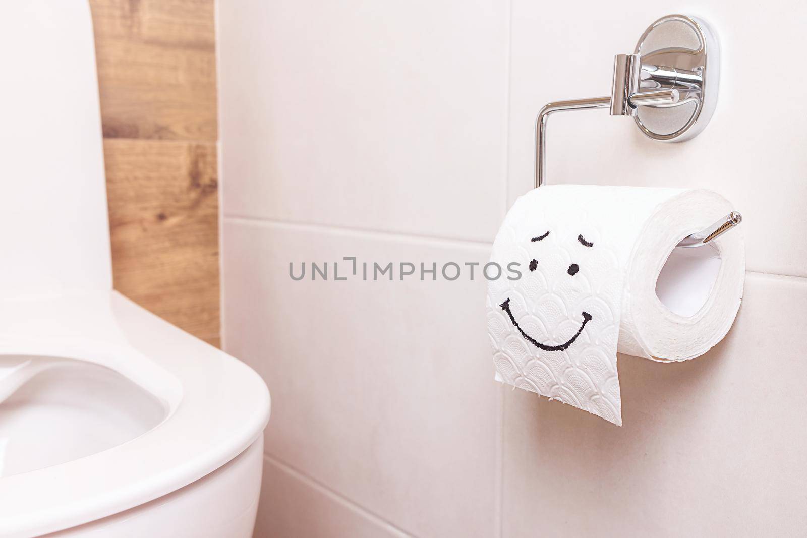 Close-up of a toilet paper roll with a funny smiley face hanging on the wall in the bathroom. The concept of good health, clean bathroom, happy life