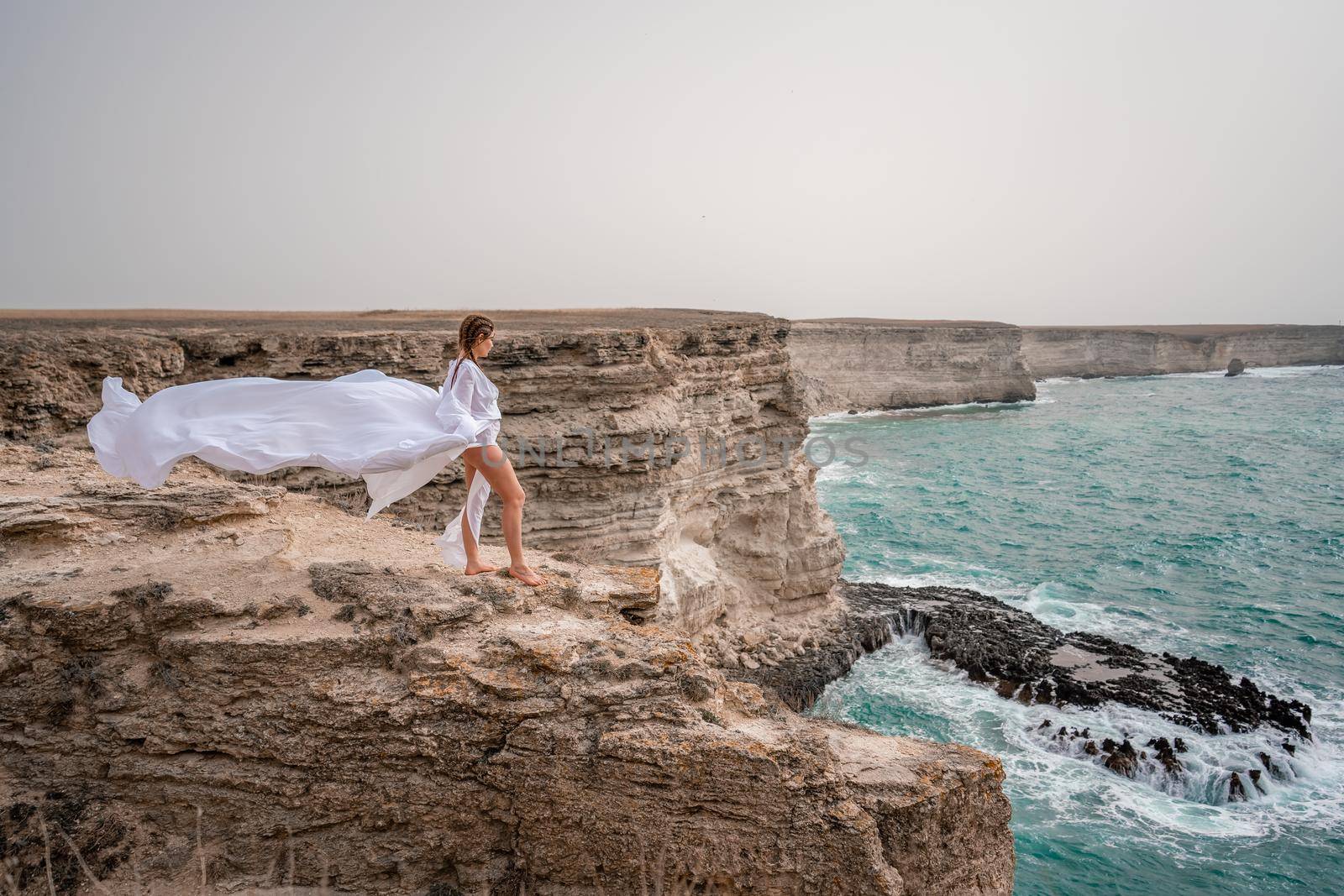 Happy freedom woman on the beach enjoying and posing in white dress over the sea. View of a girl in a fluttering white dress in the wind. Holidays, holidays at sea. by Matiunina